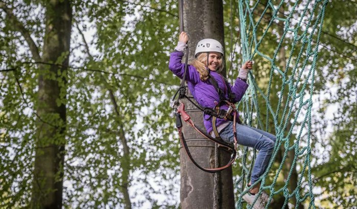 Pige -med -hjaelm -og -klatreudstyr -klatrer -op -ad -et -net -i -hochseilgarten -altenhof